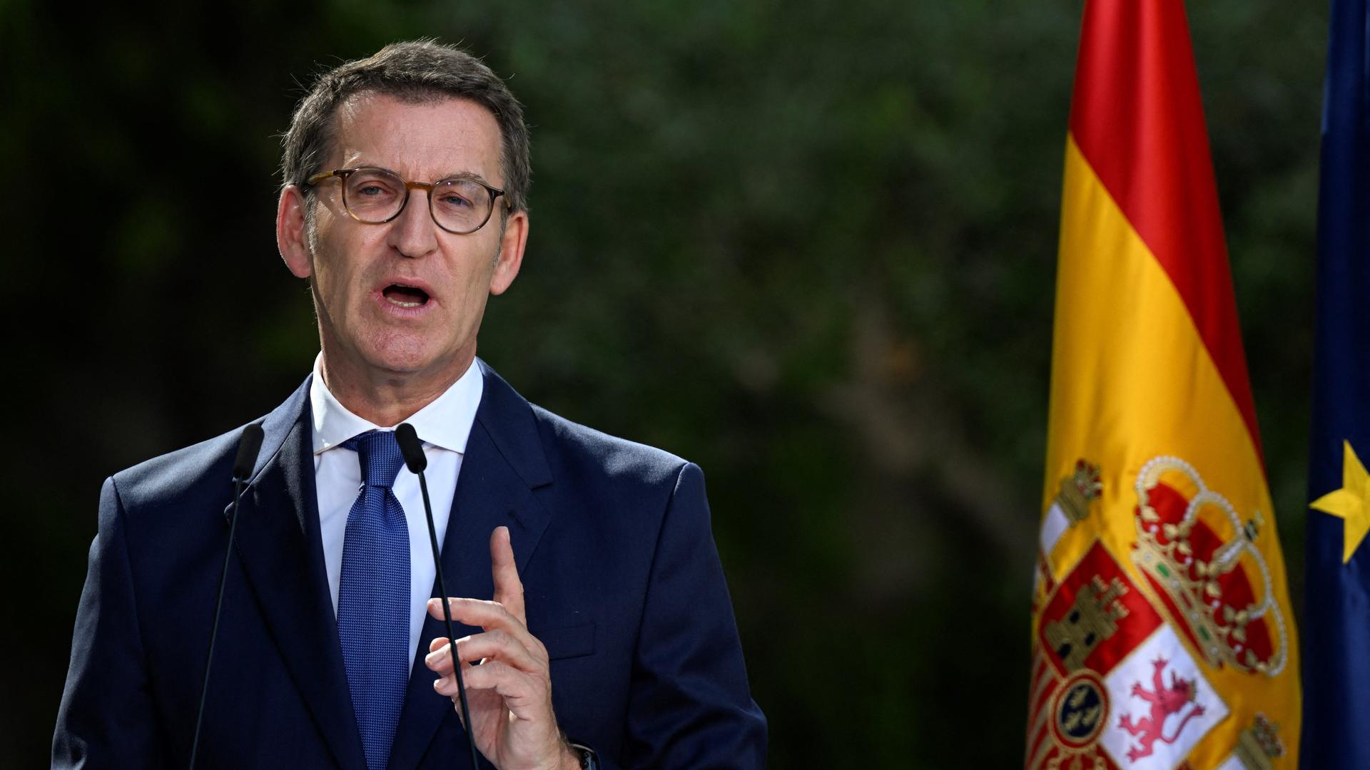 Alberto Núñez Feijóo steht mit erhobener Hand und sprechend vor einer Spanien-Flagge. Er trägt Anzug, kurze graue Haare und eine runde Brille. Alberto Núñez Feijóo steht mit erhobener Hand und sprechend vor einer Spanien-Flagge. Er trägt Anzug, kurze graue Haare und eine runde Brille.
