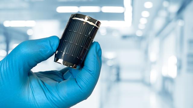 Eine Hand mit blauem Hanschuh biegt eine flexible Solarzelle der Empa