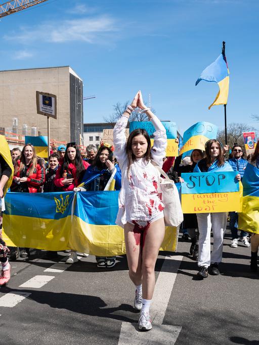 Eine junge ukrainische Frau mit gefesselten Haenden und blutgetränktem Kleid führt eine Demonstration an.