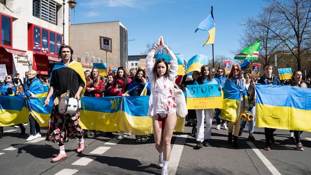 Eine junge ukrainische Frau mit gefesselten Haenden und blutgetränktem Kleid führt eine Demonstration an.