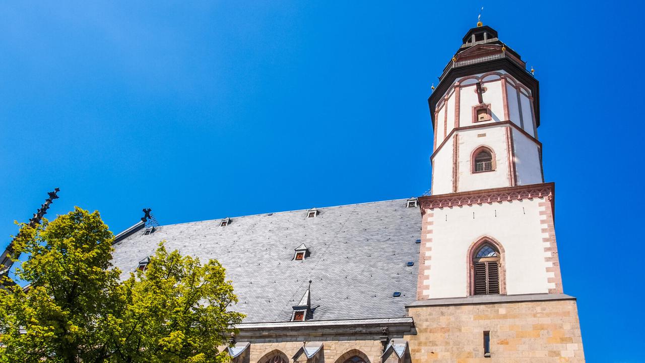 Blick von unten in die Höhe zur Turmspitze der Thomaskirche in Leipzig mit hellblauem Himmel. Blick von unten in die Höhe zur Turmspitze der Thomaskirche in Leipzig mit hellblauem Himmel.