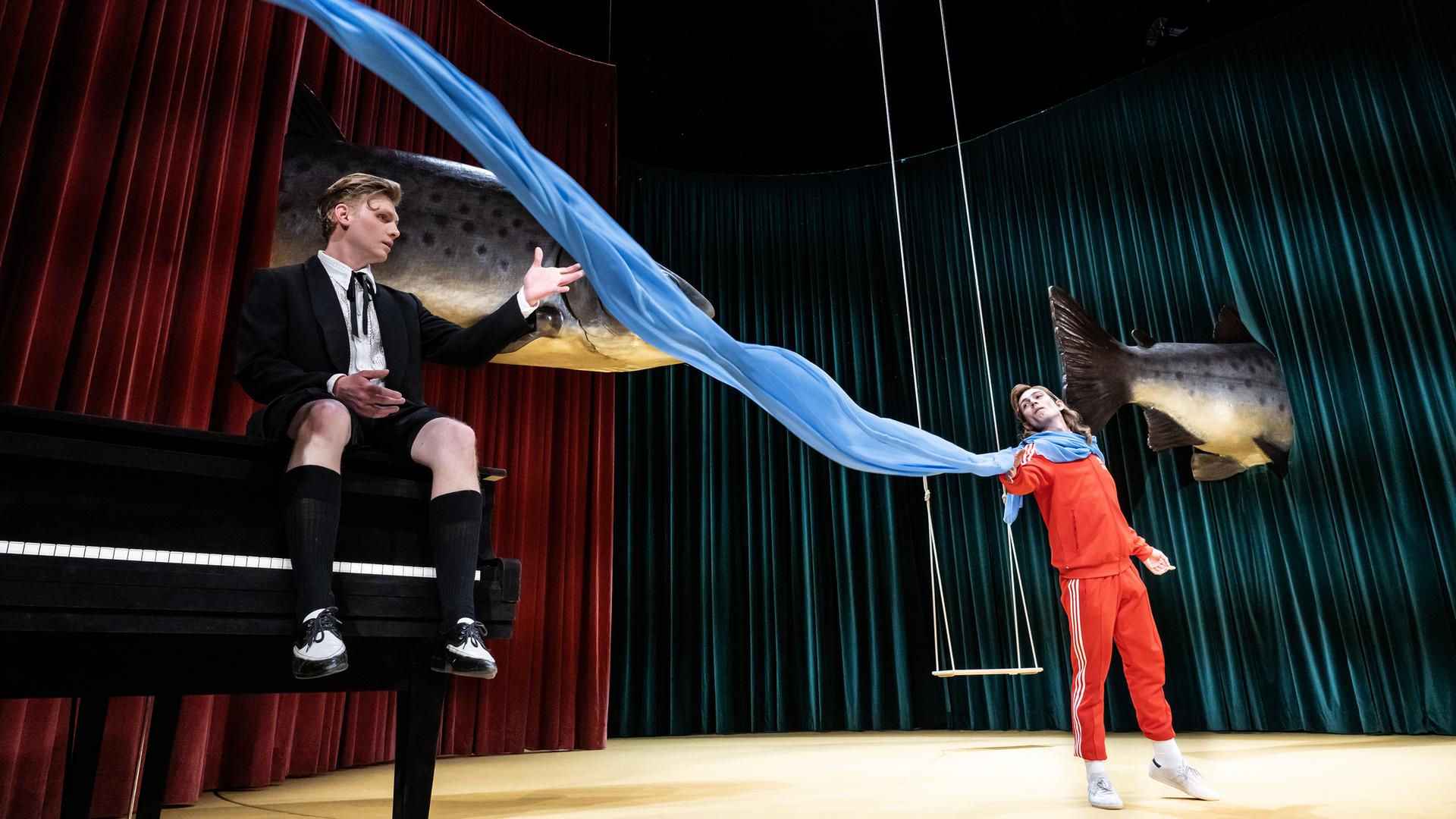 Zwischen den Schauspielern Johannes Nussbaum und Vincent zur Linden flattert ein blaues Tusch quer über die Bühne. Im Hintergrund schweben zwei riesige Fische. Zwischen den Schauspielern Johannes Nussbaum und Vincent zur Linden flattert ein blaues Tusch quer über die Bühne. Im Hintergrund schweben zwei riesige Fische.