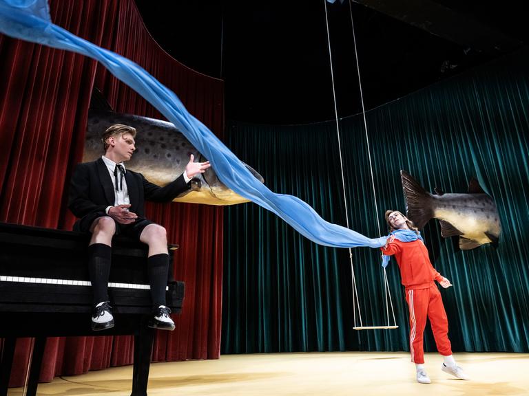 Zwischen den Schauspielern Johannes Nussbaum und Vincent zur Linden flattert ein blaues Tusch quer über die Bühne. Im Hintergrund schweben zwei riesige Fische.