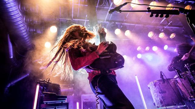 Ein Mann steht auf einer Bühne, er hälte eine E-Gitarre in der Hand und sein langes Haar schüttelt er beim Headbangen. Ein Mann steht auf einer Bühne, er hälte eine E-Gitarre in der Hand und sein langes Haar schüttelt er beim Headbangen.