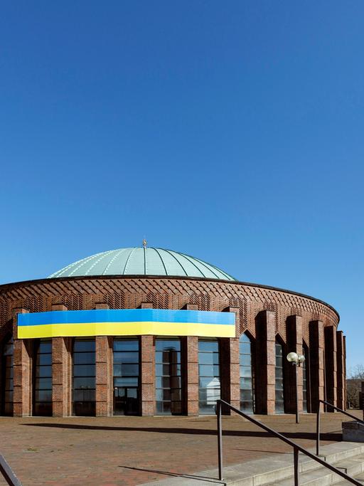 Die blau-gelbe Nationalfahne der Ukraine in an der runden Tonhalle Düsseldorf gespannt und damit weit sichtbar.