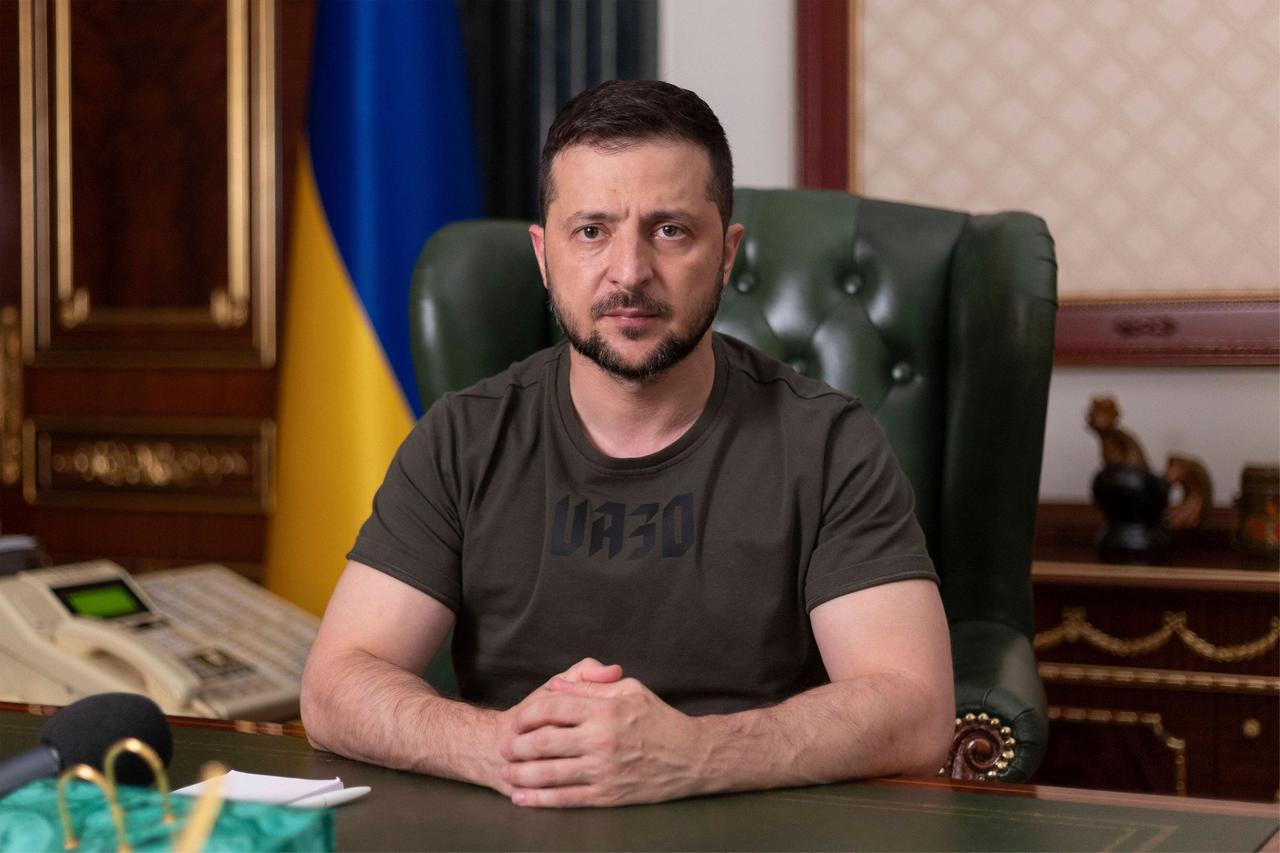 Wolodymyr Selenskyj sitzt an seinem Schreibtisch, mit ernstem Blick, die Hände gefaltet, im Hintergrund die ukrainische Fahne. Wolodymyr Selenskyj sitzt an seinem Schreibtisch, mit ernstem Blick, die Hände gefaltet, im Hintergrund die ukrainische Fahne.