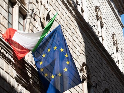 Eine italienische und eine europäische Flagge hängen an einer Hausfassade in Siena
