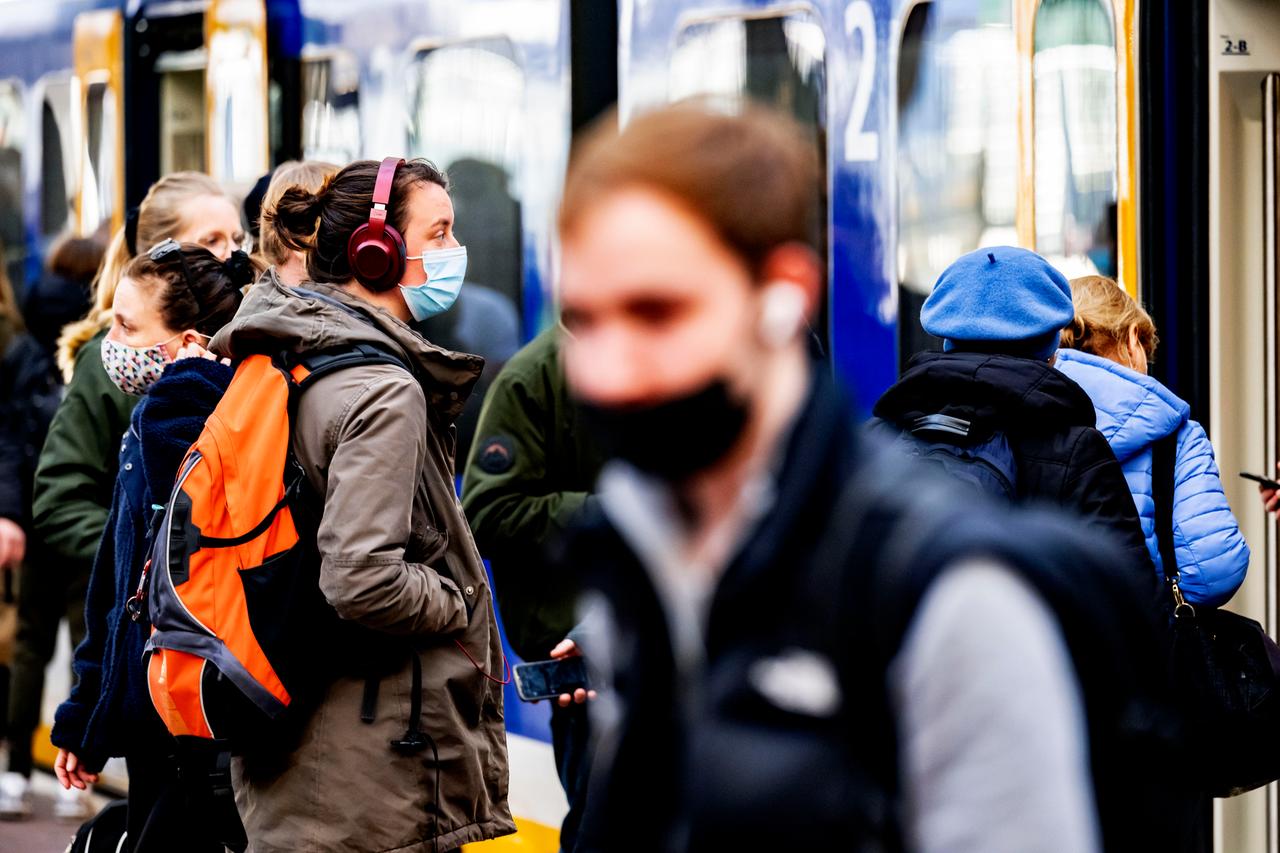 Junge Menschen stehen auf einem Bahnsteig und tragen Masken und Rucksäcke, im Hintergrund ist ein Zug zu sehen. Junge Menschen stehen auf einem Bahnsteig und tragen Masken und Rucksäcke, im Hintergrund ist ein Zug zu sehen.