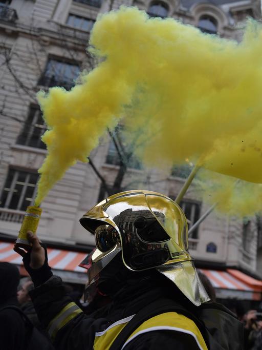 Feuerwehrleute ziehen aus Protest gegen den Staat mit Fahnen und Rauchwolken durch die Straßen von Paris.