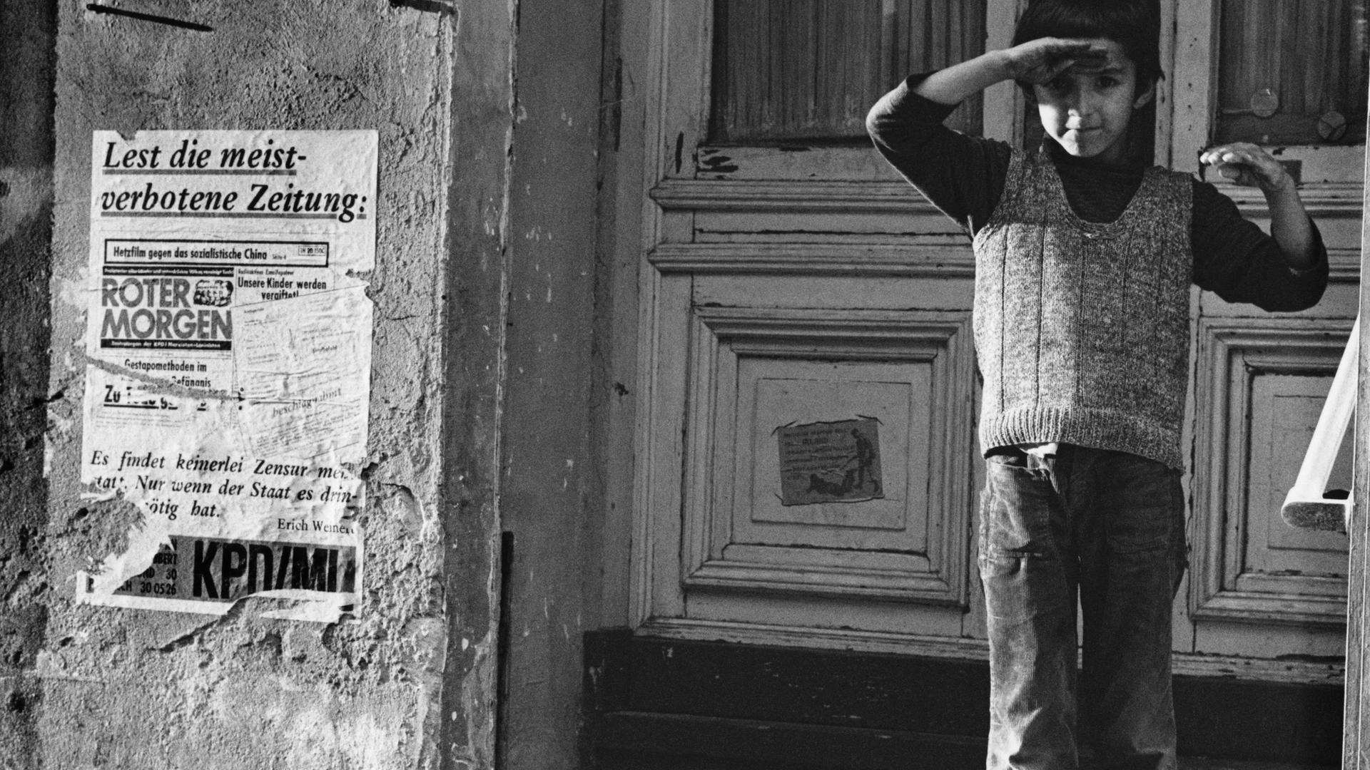 Ein türkischer Junge in Berlin-Kreuzberg 1976 steht vor einer Haustür und hält seine rechte Hand als Schutz gegen die Sonne über die Augen.