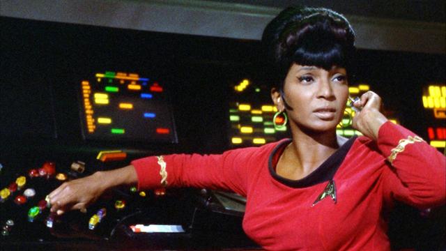 Nichelle Nichols als Lieutenant Uhura in der Serie "Raum-Schiff Enterprise" sitzt in einer roten Uniform vor einem Schalt-Pult mit bunten Lichtern.