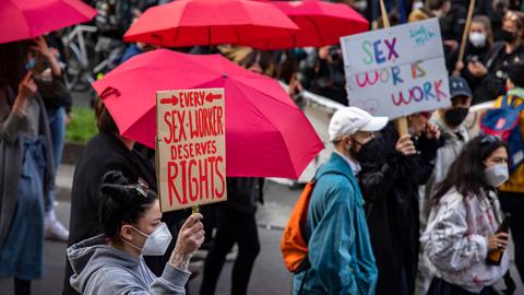 Auf einer Demonstration hält eine Frau ein Schild mit der Aufschrift "Every sex worker deserves rights". Im Hintergrund sind rote Regenschirme zu sehen.