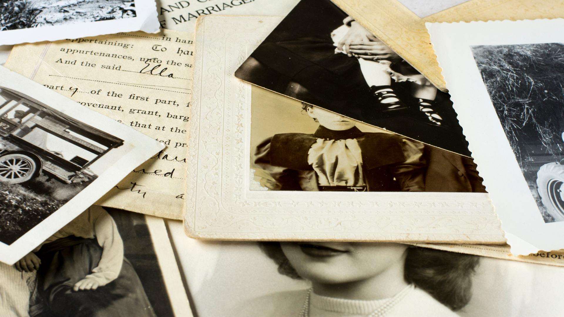Auf einem Tisch liegen mehrere alte Familienfotos und Dokumente durcheinander.