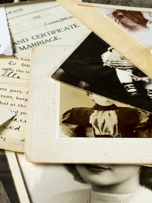 Auf einem Tisch liegen mehrere alte Familienfotos und Dokumente durcheinander.