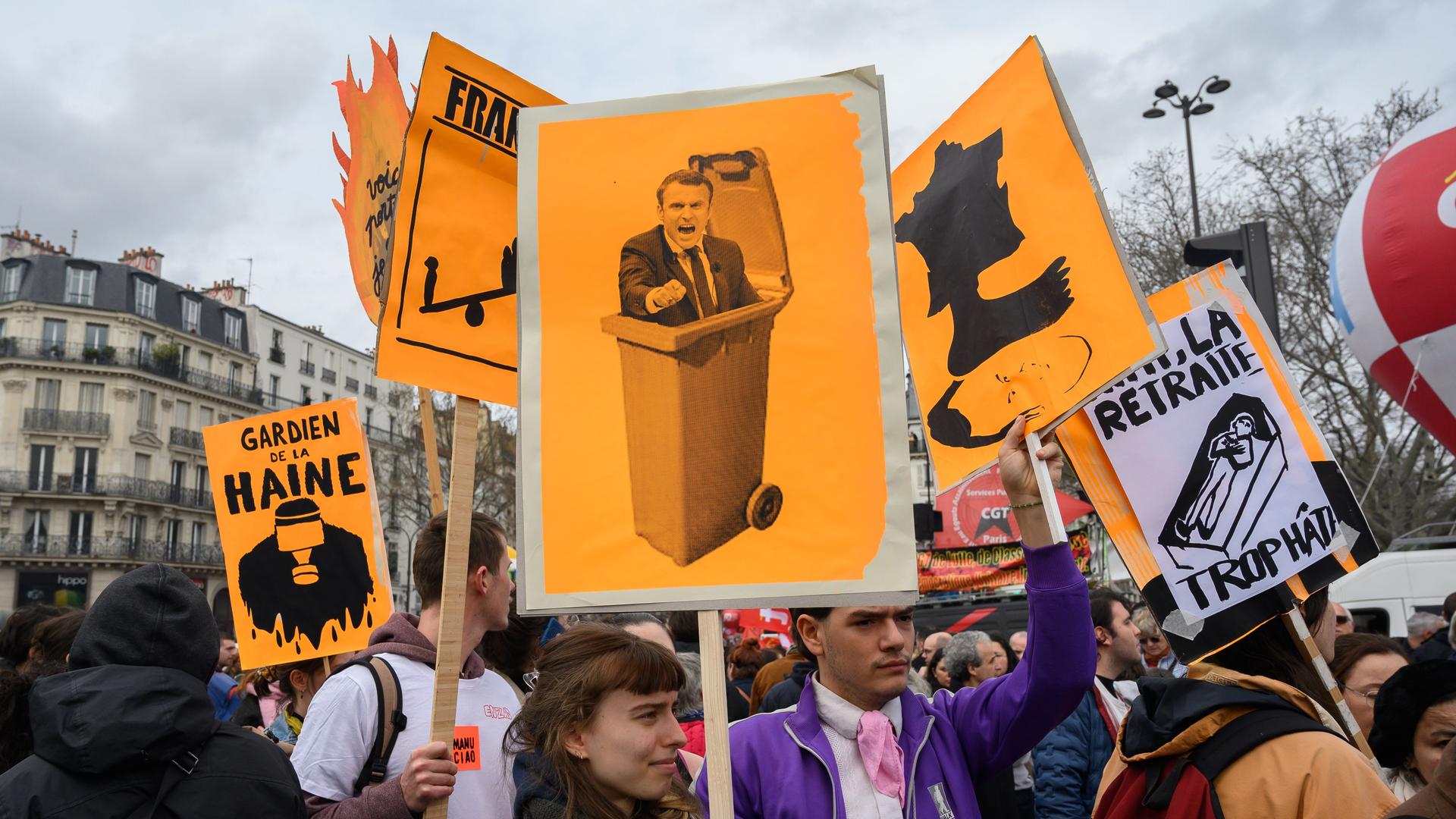 Proteste gegen die umstrittene Rentenreform in Frankreich. Demonstranten halten Schilder und Transparente, auf einem ist der französische Präsident Emmanuel Macron zu sehen, der in einer Mülltonne steckt. Proteste gegen die umstrittene Rentenreform in Frankreich. Demonstranten halten Schilder und Transparente, auf einem ist der französische Präsident Emmanuel Macron zu sehen, der in einer Mülltonne steckt.