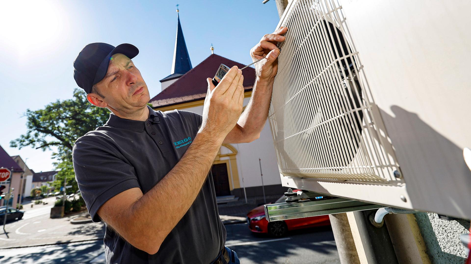 Klima- und Kältetechniker Stefan Häfner misst die Austrittstemperatur aus einer Klimaanlage bei der Wartung in der prallen Sonne.