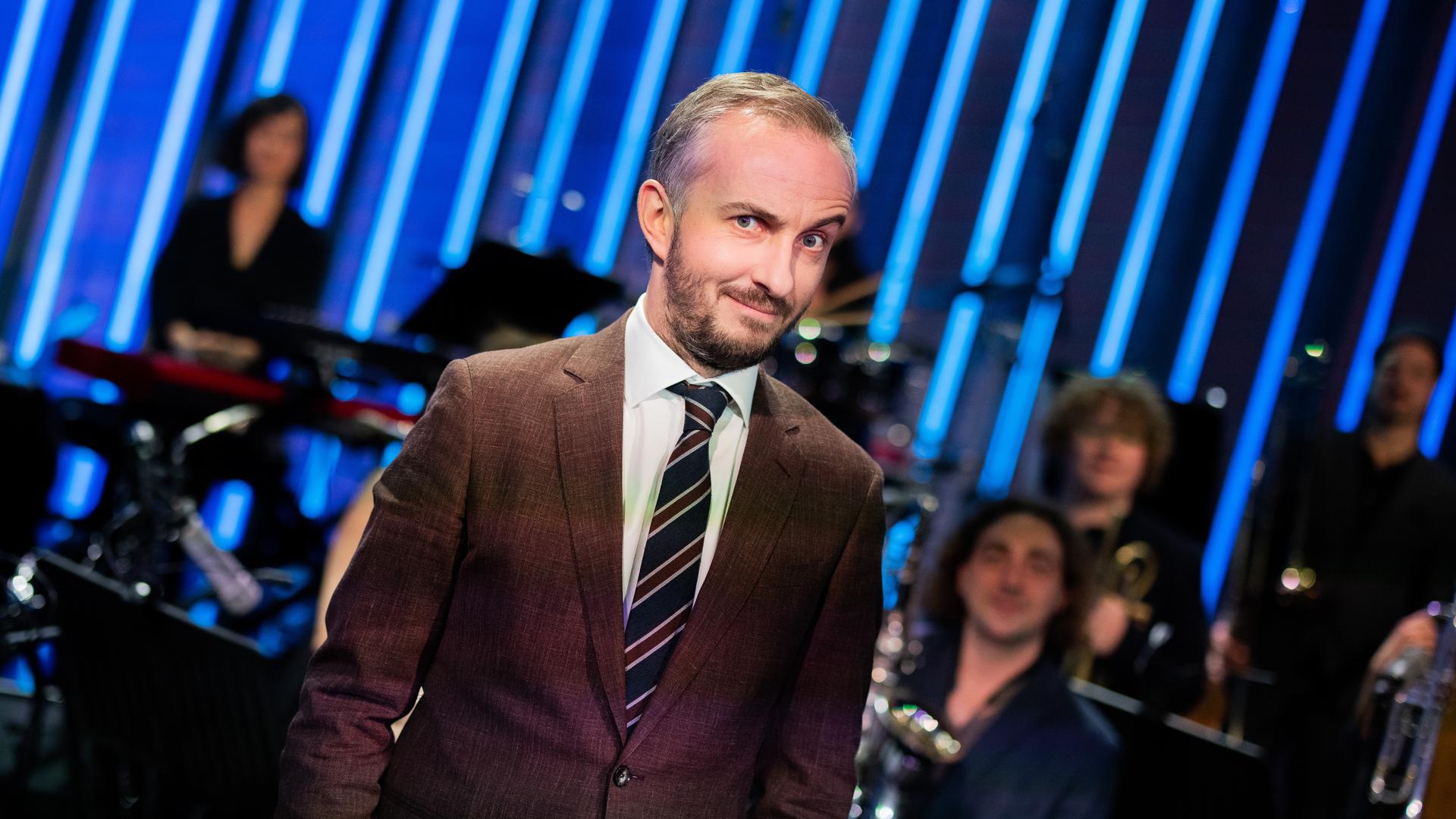 Jan Böhmermann steht im Studio des ZDF Magazin Royal vor seinem Orchester und macht eine ironische Grimasse mit hochgezogener Augenbraue. Jan Böhmermann steht im Studio des ZDF Magazin Royal vor seinem Orchester und macht eine ironische Grimasse mit hochgezogener Augenbraue.