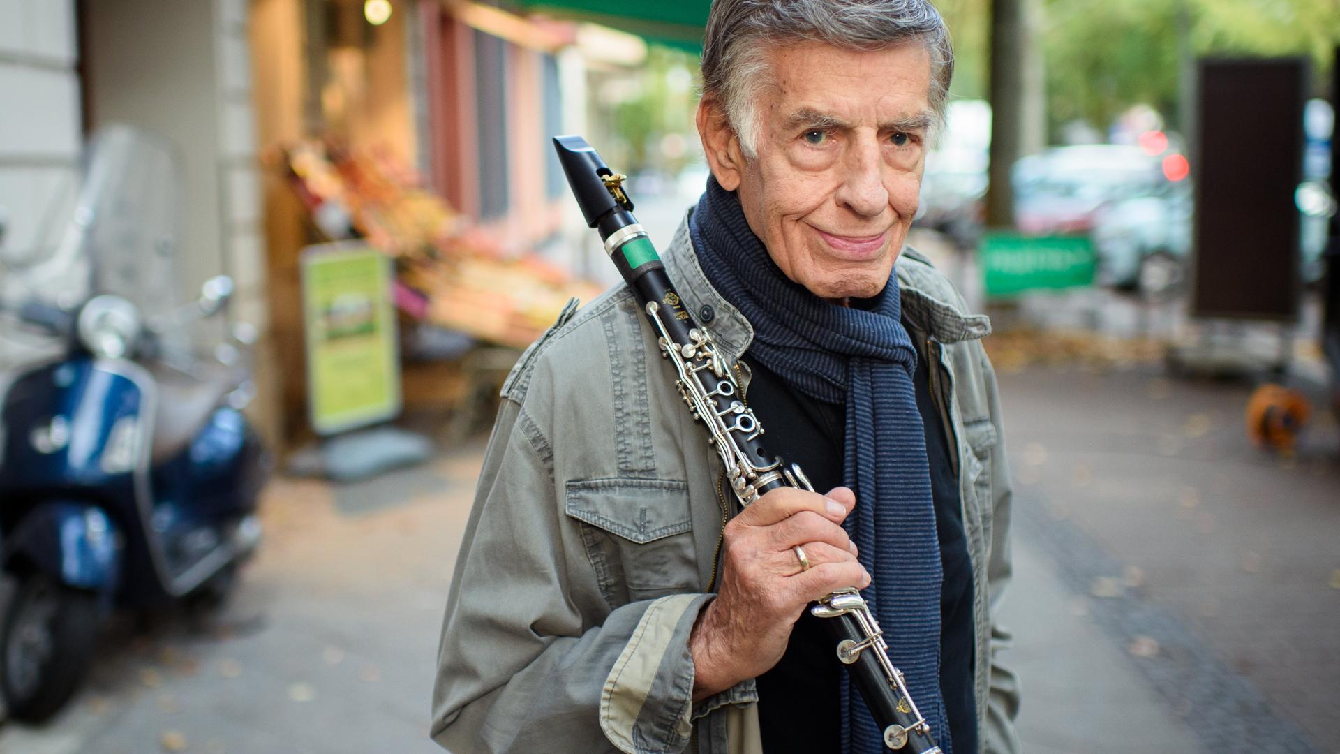 Rolf Kühn, Jazzmusiker und Komponist, steht im Berliner Bezirk Charlottenburg auf einem Gehweg und hält seine Klarinette in der Hand. Er hat graue, zur Seite gekämmte Haare und trägt einen blauen Schal um den Hals. Rolf Kühn, Jazzmusiker und Komponist, steht im Berliner Bezirk Charlottenburg auf einem Gehweg und hält seine Klarinette in der Hand. Er hat graue, zur Seite gekämmte Haare und trägt einen blauen Schal um den Hals.