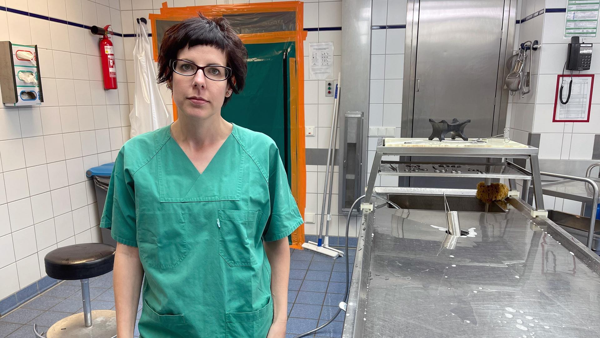 Die Rechtsmedizinerin Sarah Kölzer steht in einem Gerichtsmedizinischen Institut, sie trägt einen grünen Operationskittel.