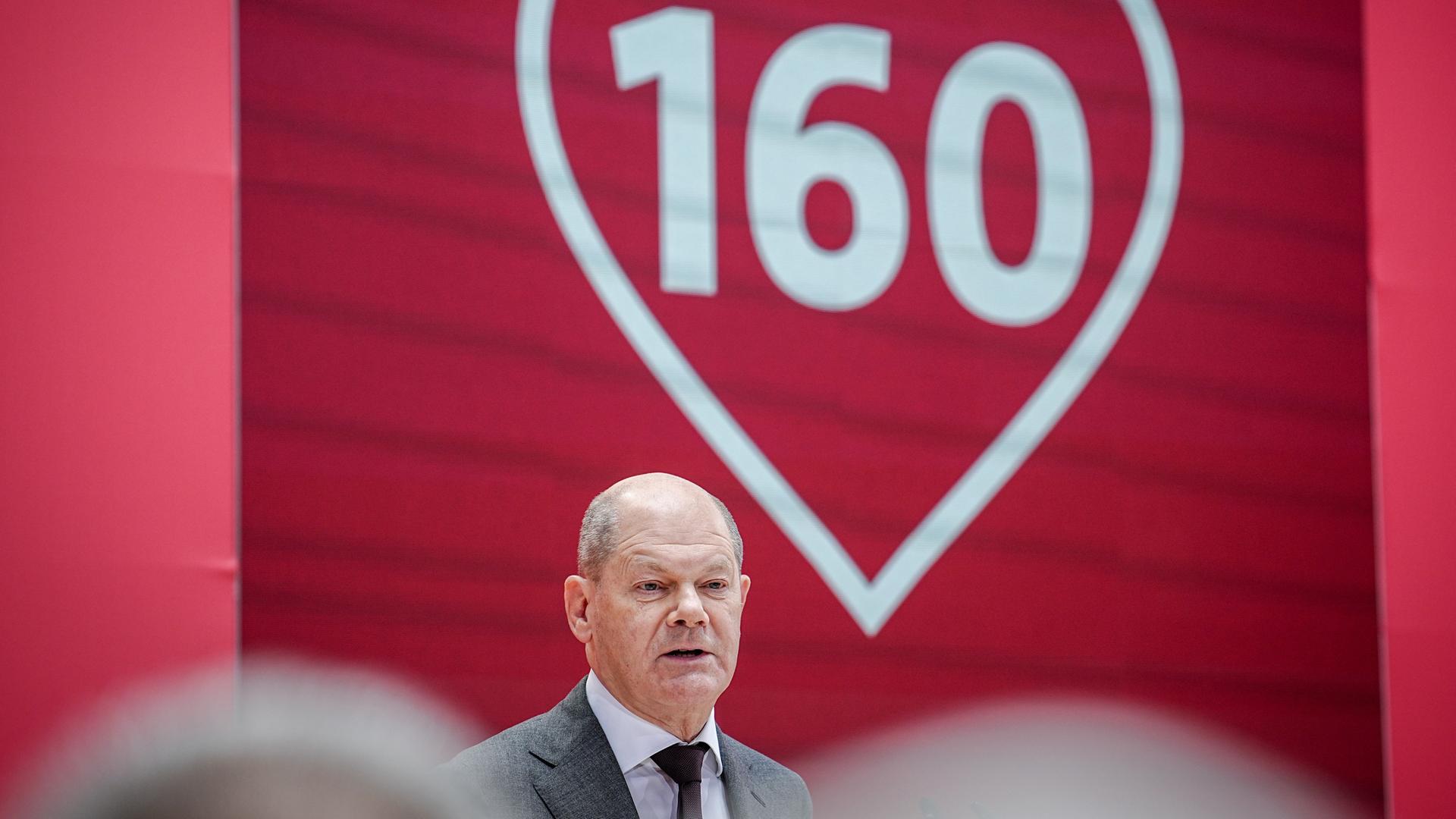 Bundes-Kanzler Olaf Scholz spricht auf dem Fest-Akt zu 160 Jahren SPD. Er steht vor einem Herz mit der Zahl 160 darin.