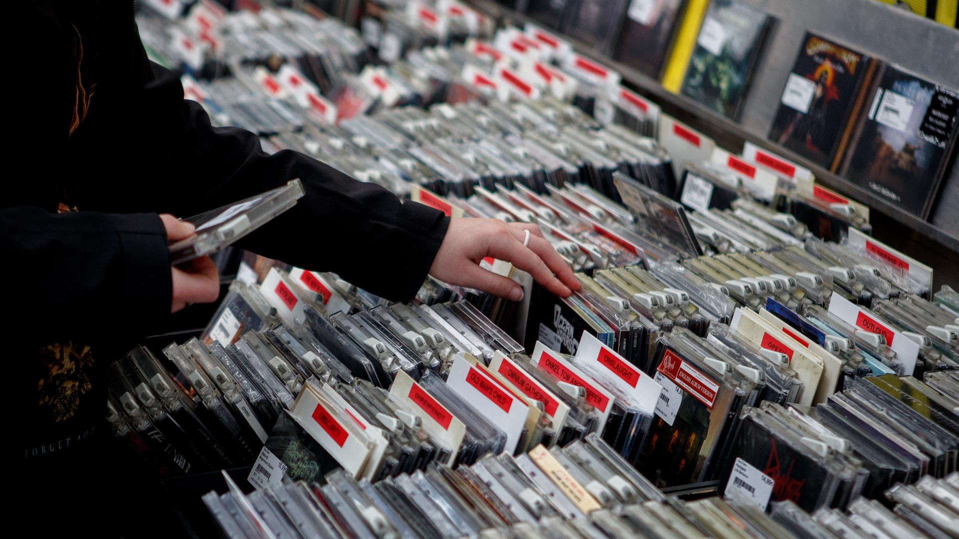 Eine Person gleitet in einem CD-Geschäft mit dem Finger durch das Angebot.