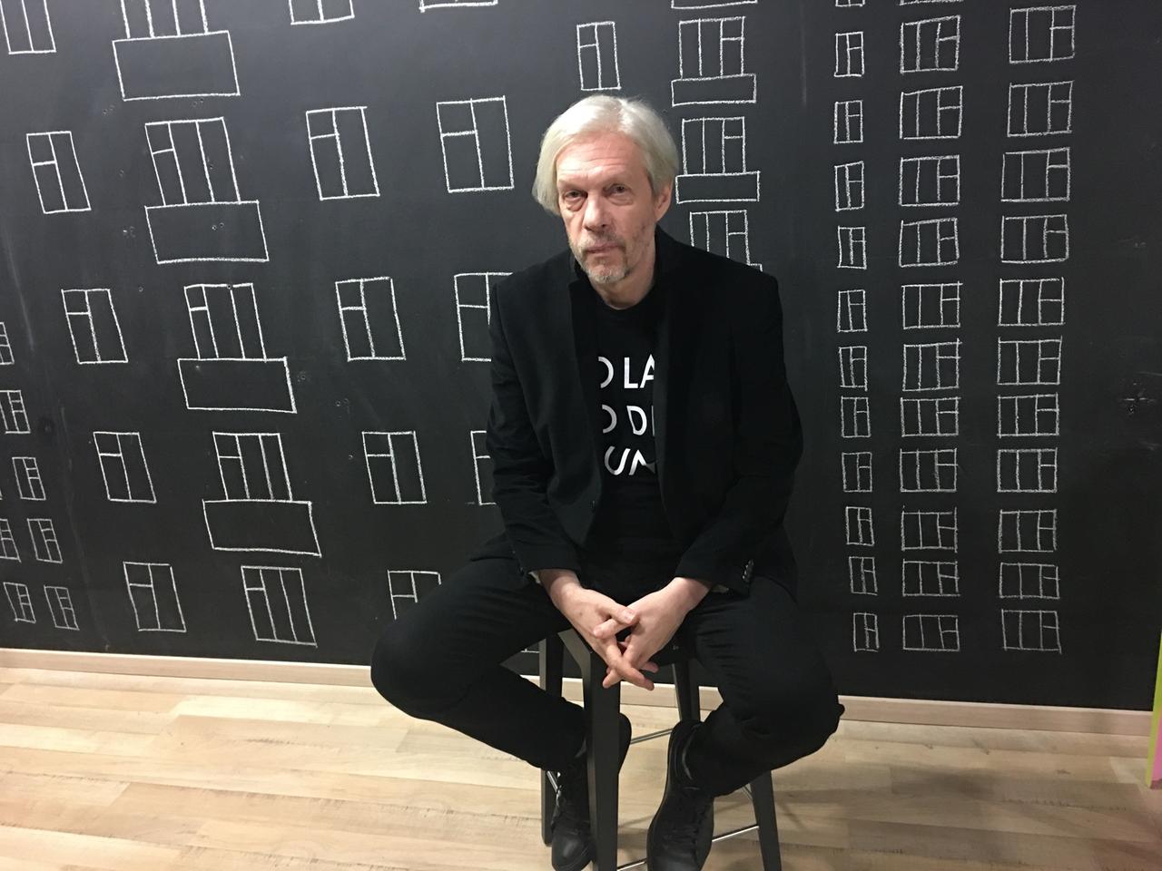 Ein Mann mit langen weißen Haaren sitzt auf einem Barhocker und schaut in die Kamera: Maxim Schbankov Ein Mann mit langen weißen Haaren sitzt auf einem Barhocker und schaut in die Kamera: Maxim Schbankov
