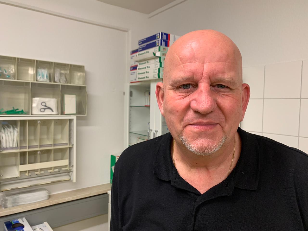 Krankenpfleger Amadeus von der Oelsnitz, mittelalt, Glatze, schwarzes T-Shirt, im Krankenzimmer des Gesundheitszentrums Krankenpfleger Amadeus von der Oelsnitz, mittelalt, Glatze, schwarzes T-Shirt, im Krankenzimmer des Gesundheitszentrums