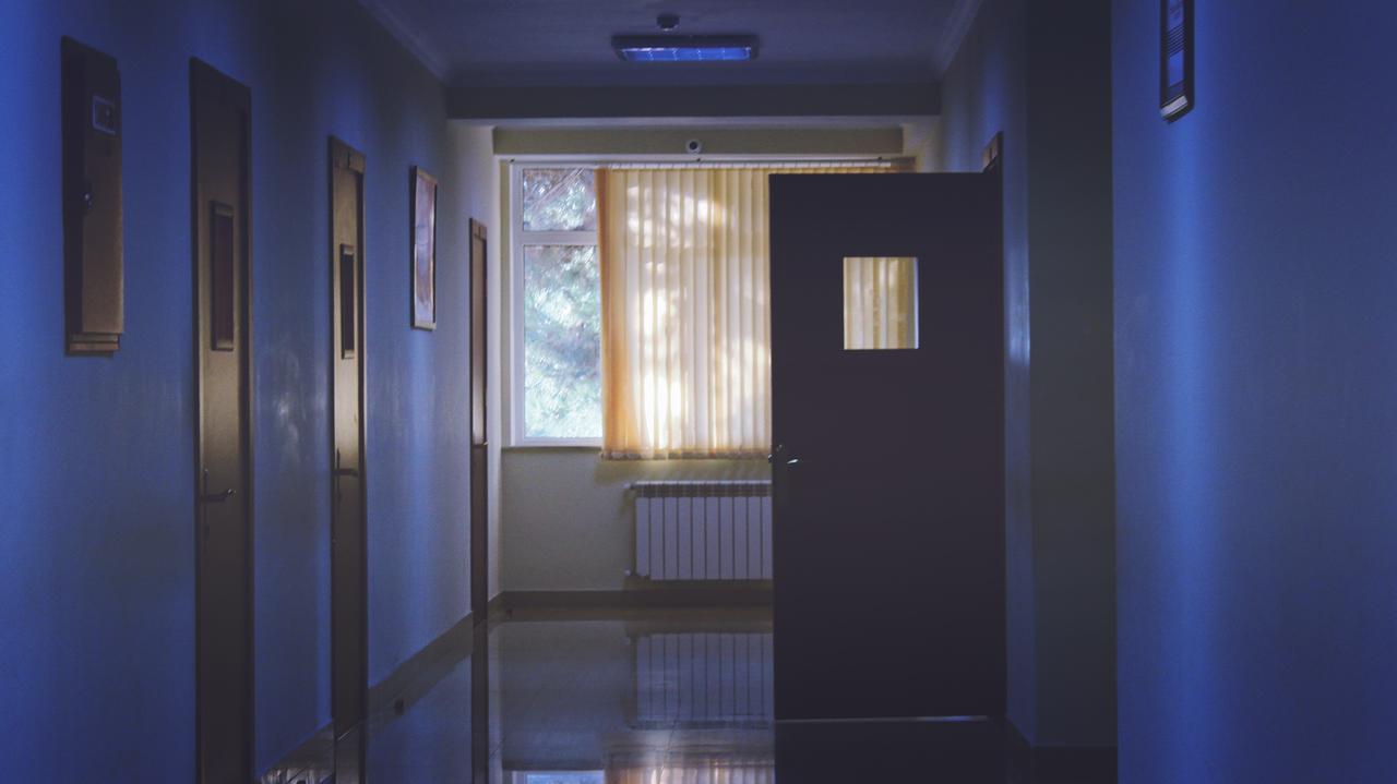 In einem düsteren Krankenhausflur steht eine Tür offen.