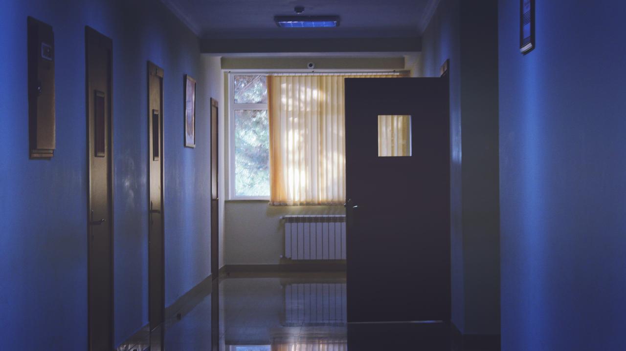 In einem düsteren Krankenhausflur steht eine Tür offen. In einem düsteren Krankenhausflur steht eine Tür offen.