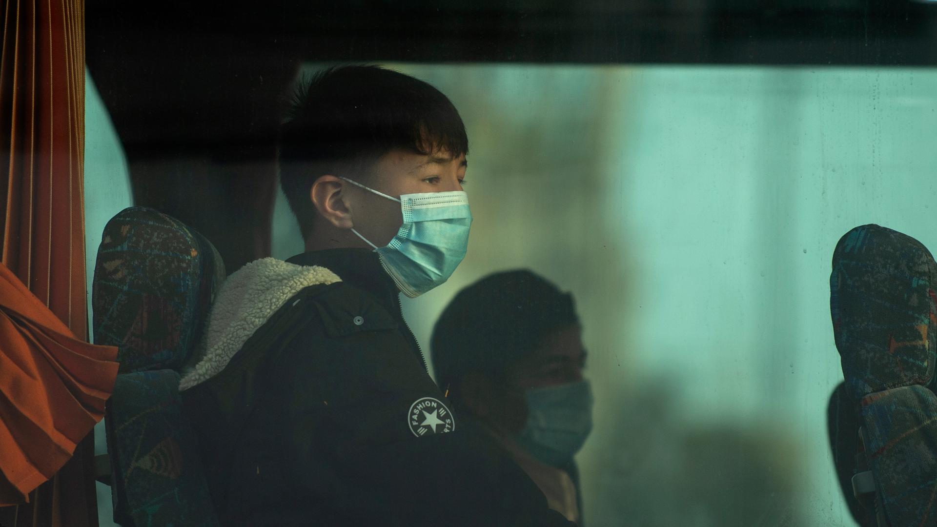 Eine Gruppe unbegleiteter Kinder tragen Schutzmasken und sind durch das Fenster eines Busses zu sehen. Eine Gruppe unbegleiteter Kinder tragen Schutzmasken und sind durch das Fenster eines Busses zu sehen.