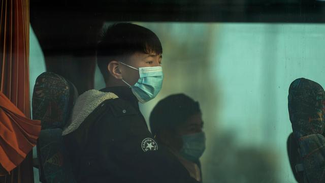 Eine Gruppe unbegleiteter Kinder tragen Schutzmasken und sind durch das Fenster eines Busses zu sehen. 