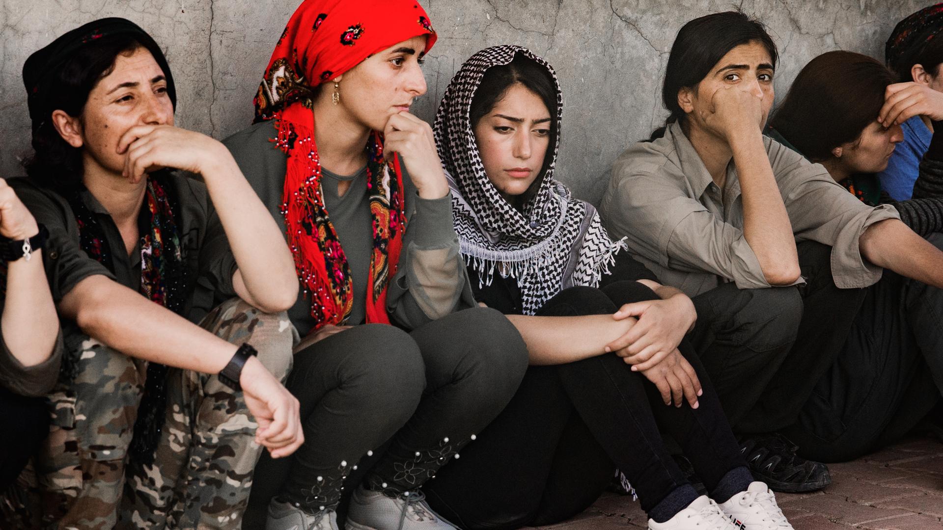 Junge Frauen sitzen nebeneinander an eine Wand gelehnt auf dem Boden.