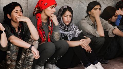 Junge Frauen sitzen nebeneinander an eine Wand gelehnt auf dem Boden.