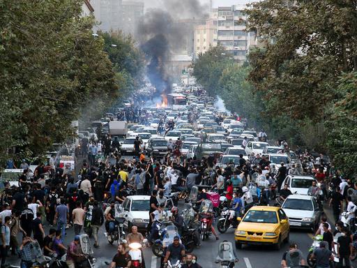 Demonstranten blockieren eine Straße in Teheran, Rachwolken sind zu sehen