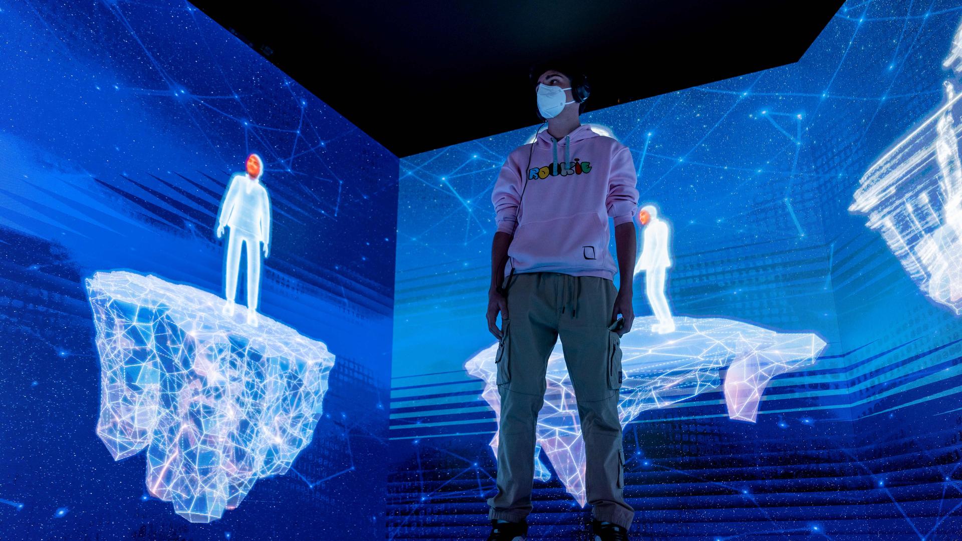 Ein Junge steht mit seinem Avatar in einer virtuellen, blau leuchtenden Landschaft. Ein Junge steht mit seinem Avatar in einer virtuellen, blau leuchtenden Landschaft.