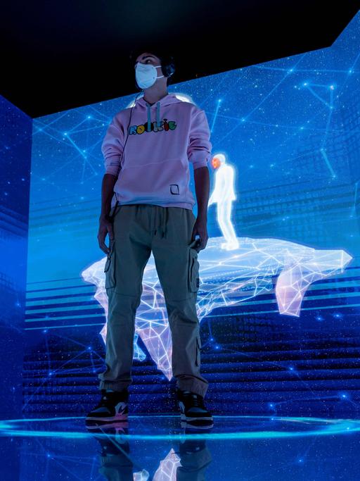 Ein Junge steht mit seinem Avatar in einer virtuellen, blau leuchtenden Landschaft.