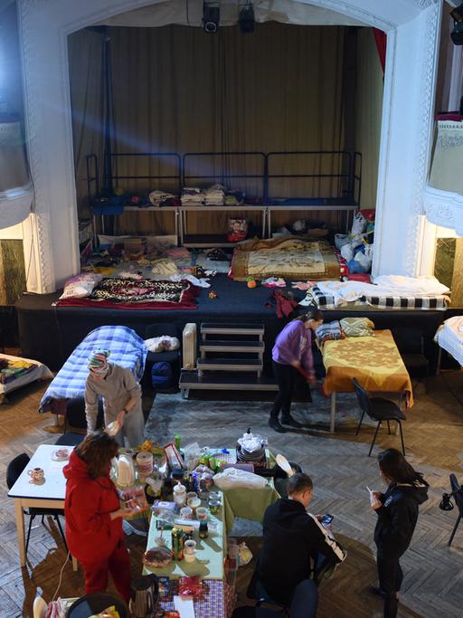 Im Zuschauerraum eines Theatersaals haben sich Gefluechtete notdürftig mit Tischen und Betten eingerichtet.