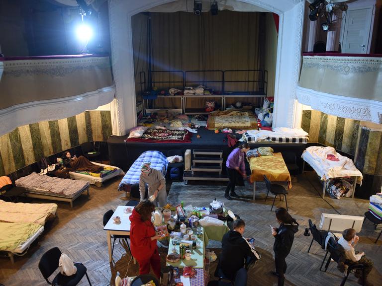 Im Zuschauerraum eines Theatersaals haben sich Gefluechtete notdürftig mit Tischen und Betten eingerichtet.