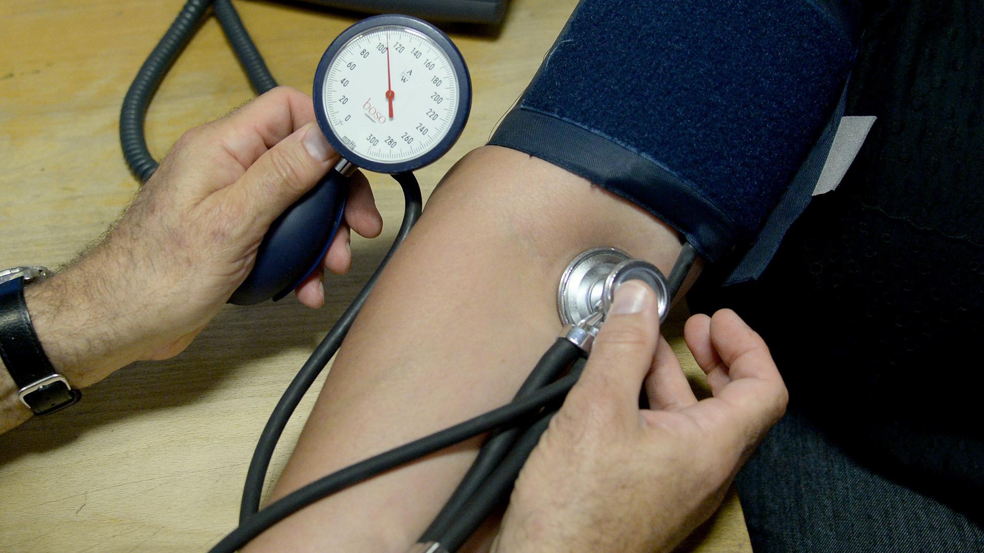 Am Arm einer Patientin wird der Blutdruck gemessen. Der Arm ist von einer Manschette umschlossen. Am Arm einer Patientin wird der Blutdruck gemessen. Der Arm ist von einer Manschette umschlossen.