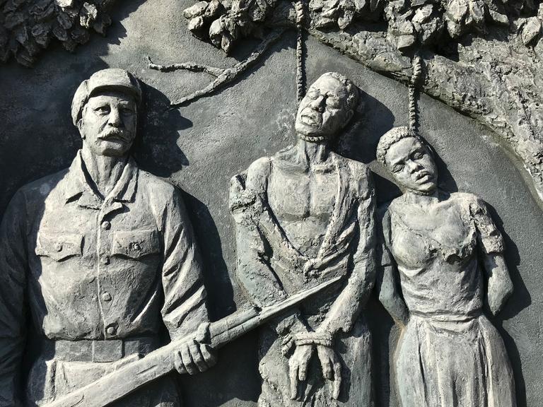 Ein Denkmal zur Erinnerung an den von deutschen Kolonialtruppen begangenen Völkermord an den Herero und Nama zeigt Gehängte neben einem schnauzbärtigen Soldaten.