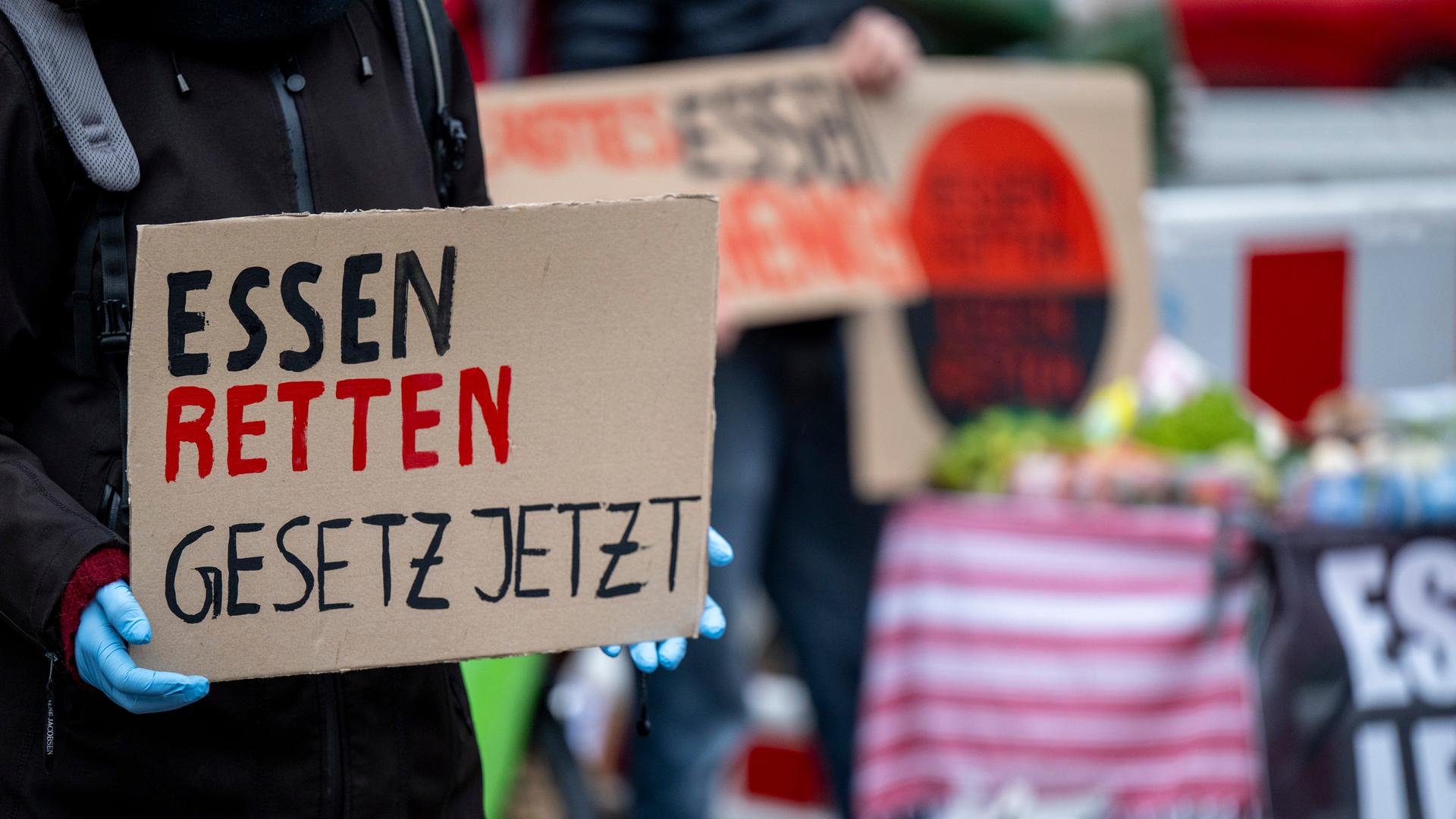 Eine Klimaaktivistin von der Initiative "Aufstand der letzten Generation" hält ein Schild mit der Aufschrift âEssen retten - Gesetz jetztâ, während im Hintergrund weitere Aktivisten weggeworfene Lebensmittel an Passanten verteilen. Die Lebensmittel werden im Rahmen der Aktion für ein âEssen-Retten-Gesetzâ und Agrarwende verschenkt. Eine Klimaaktivistin von der Initiative "Aufstand der letzten Generation" hält ein Schild mit der Aufschrift âEssen retten - Gesetz jetztâ, während im Hintergrund weitere Aktivisten weggeworfene Lebensmittel an Passanten verteilen. Die Lebensmittel werden im Rahmen der Aktion für ein âEssen-Retten-Gesetzâ und Agrarwende verschenkt.
