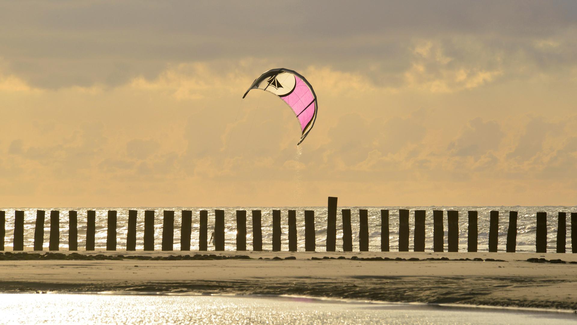 Bunter Lenkdrachen hinter Pfahlreihe am Strand im Abendlicht in Friesland. Bunter Lenkdrachen hinter Pfahlreihe am Strand im Abendlicht in Friesland.