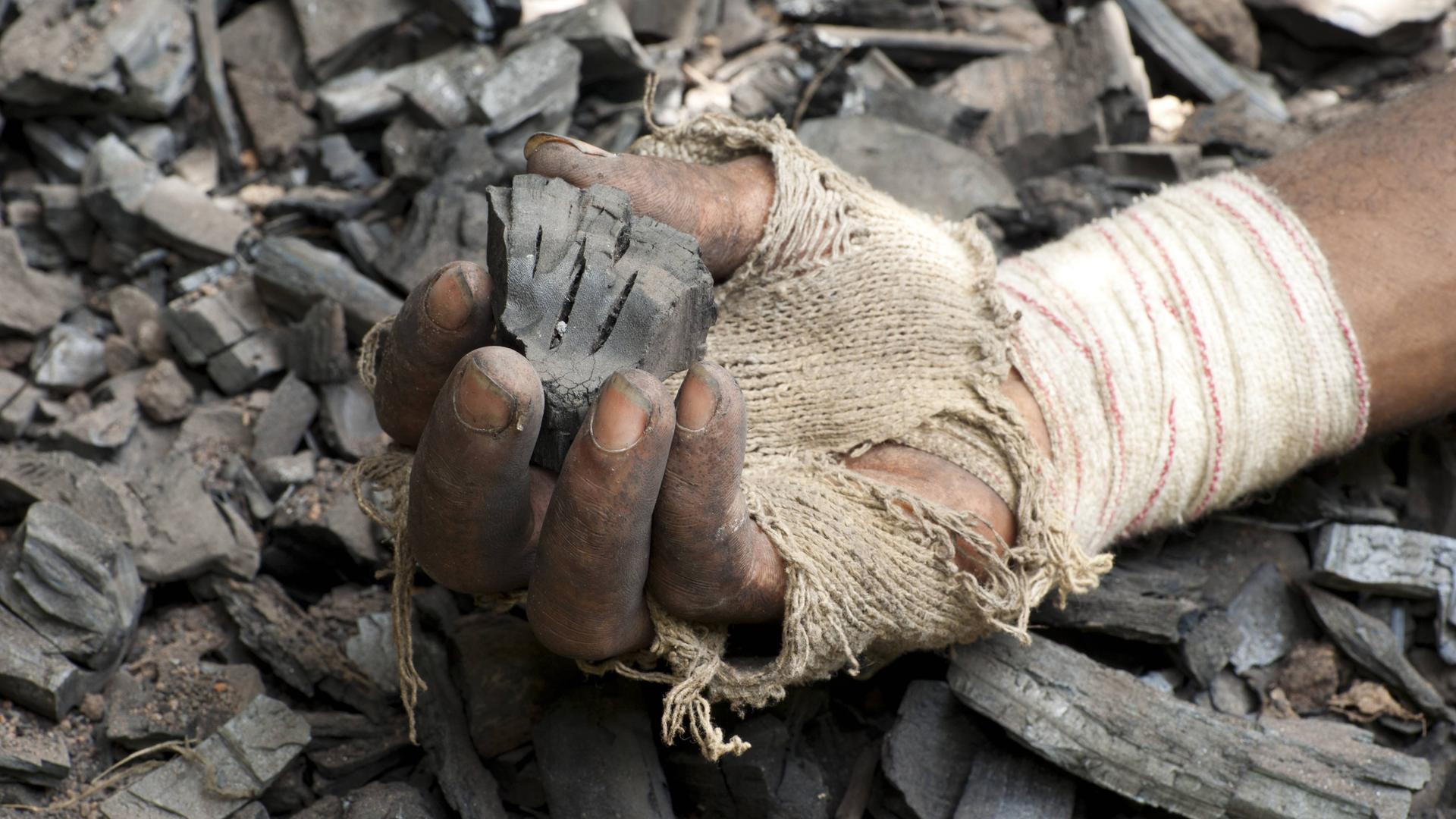Die Hand eines Mannes hält ein Stück Holzkohle Die Hand eines Mannes hält ein Stück Holzkohle
