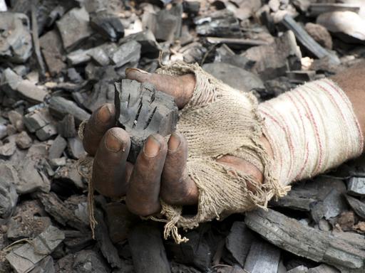 Die Hand eines Mannes hält ein Stück Holzkohle
