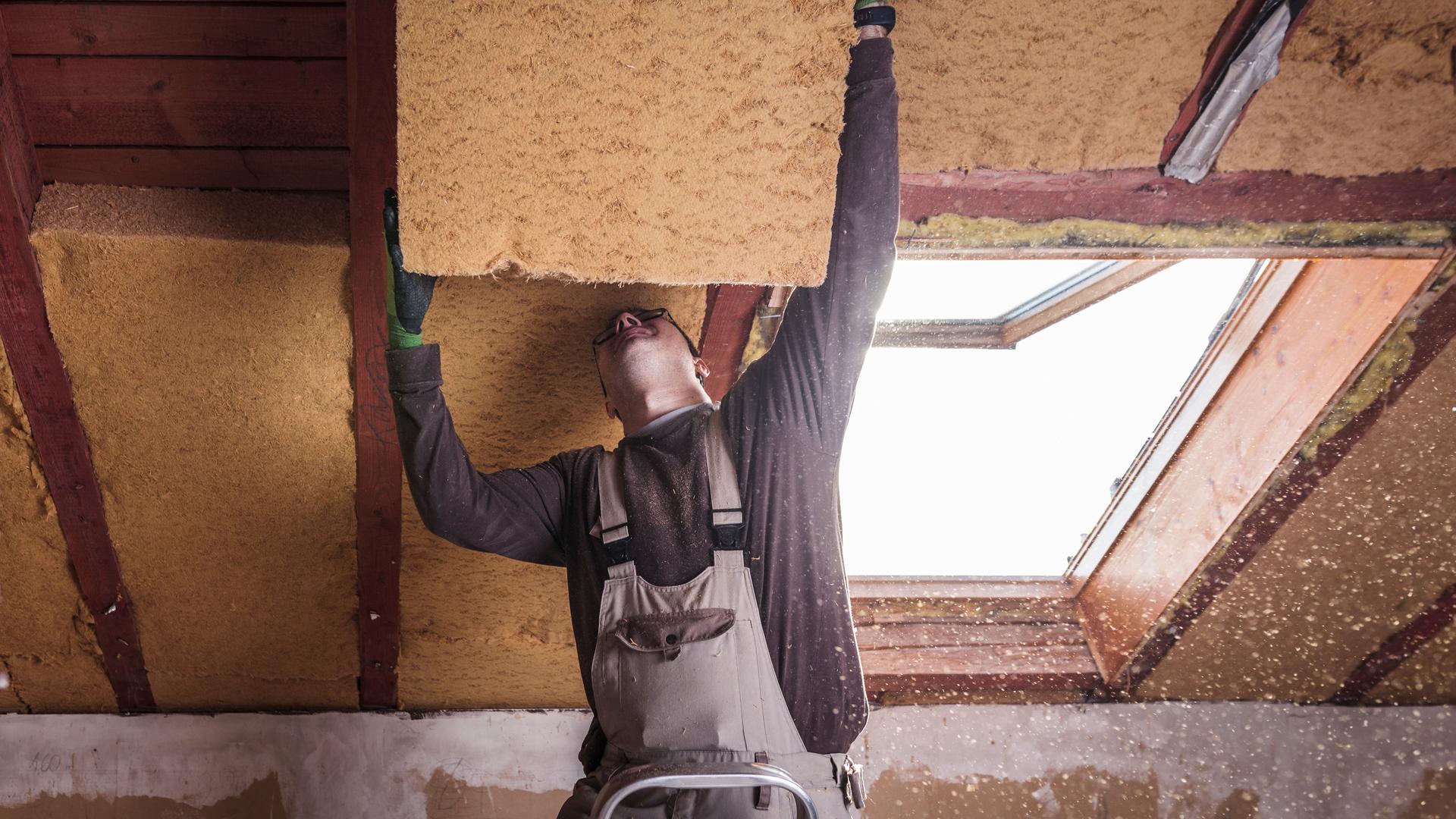 Wärmedämmung an einem Haus, ein Handwerker bringt eine Dämmplatte an einem Dach an.