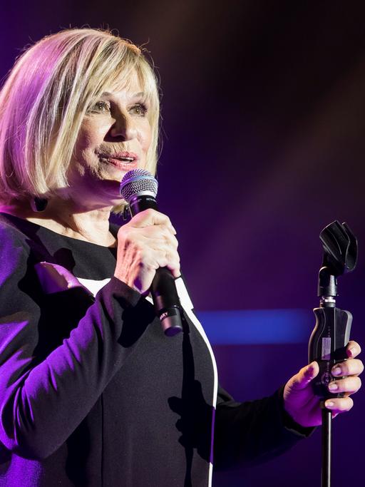 Mary Roos bei einem Konzert im Berliner Admiralspalast 2018. Sie hat ein Mikrofon in der Hand, der Hintergrund leuchtet blau.