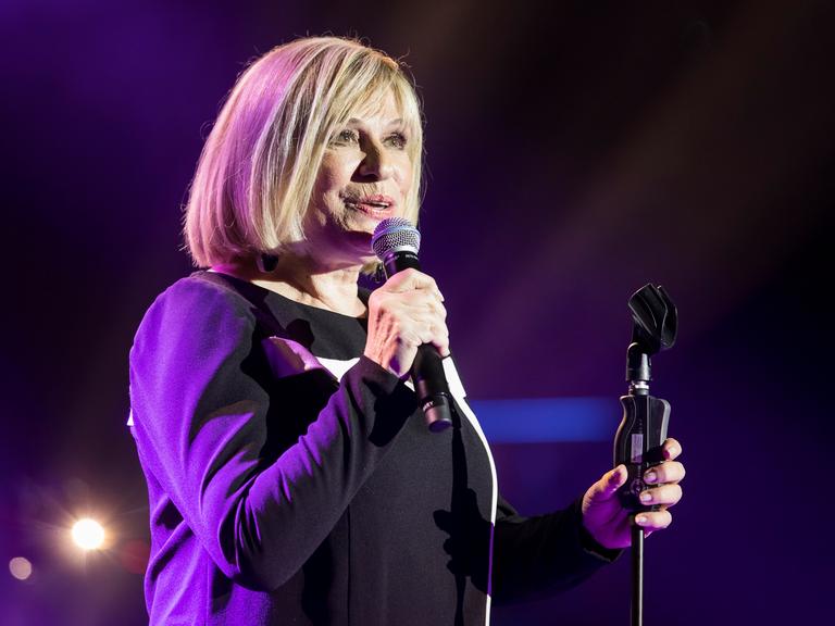 Mary Roos bei einem Konzert im Berliner Admiralspalast 2018. Sie hat ein Mikrofon in der Hand, der Hintergrund leuchtet blau.