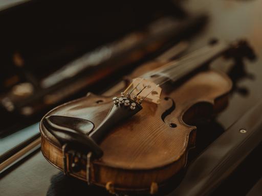Wiederentdeckte Instrumente werden  zu neuem musikalischen Leben erweckt. Zu sehen: Eine kleine Geige liegt auf einem Tisch, dahinter der geöffbete Geigenkasten.