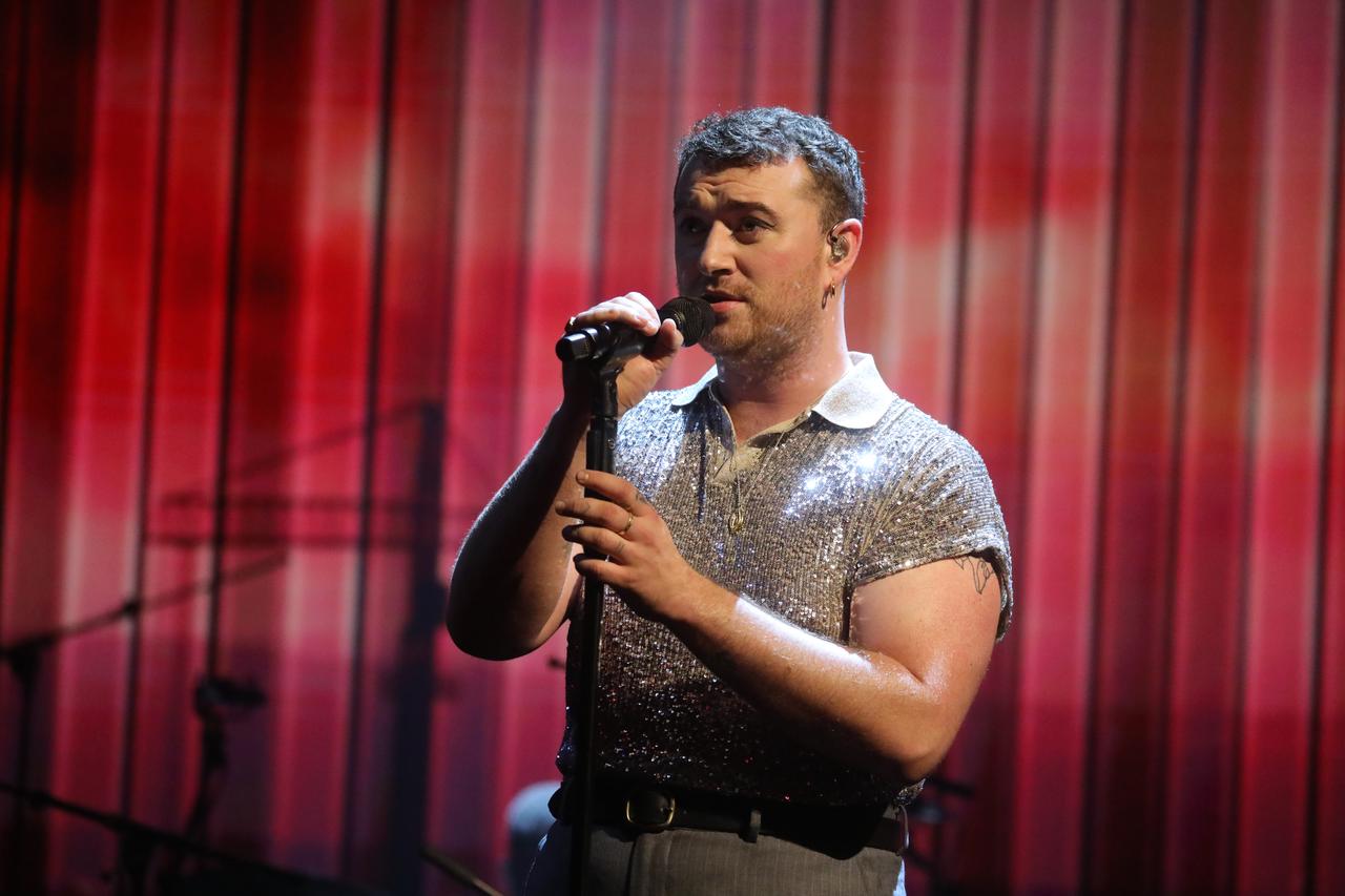 Sam Smith singt vor einem roten Vorhang in ein Mikrofon.
