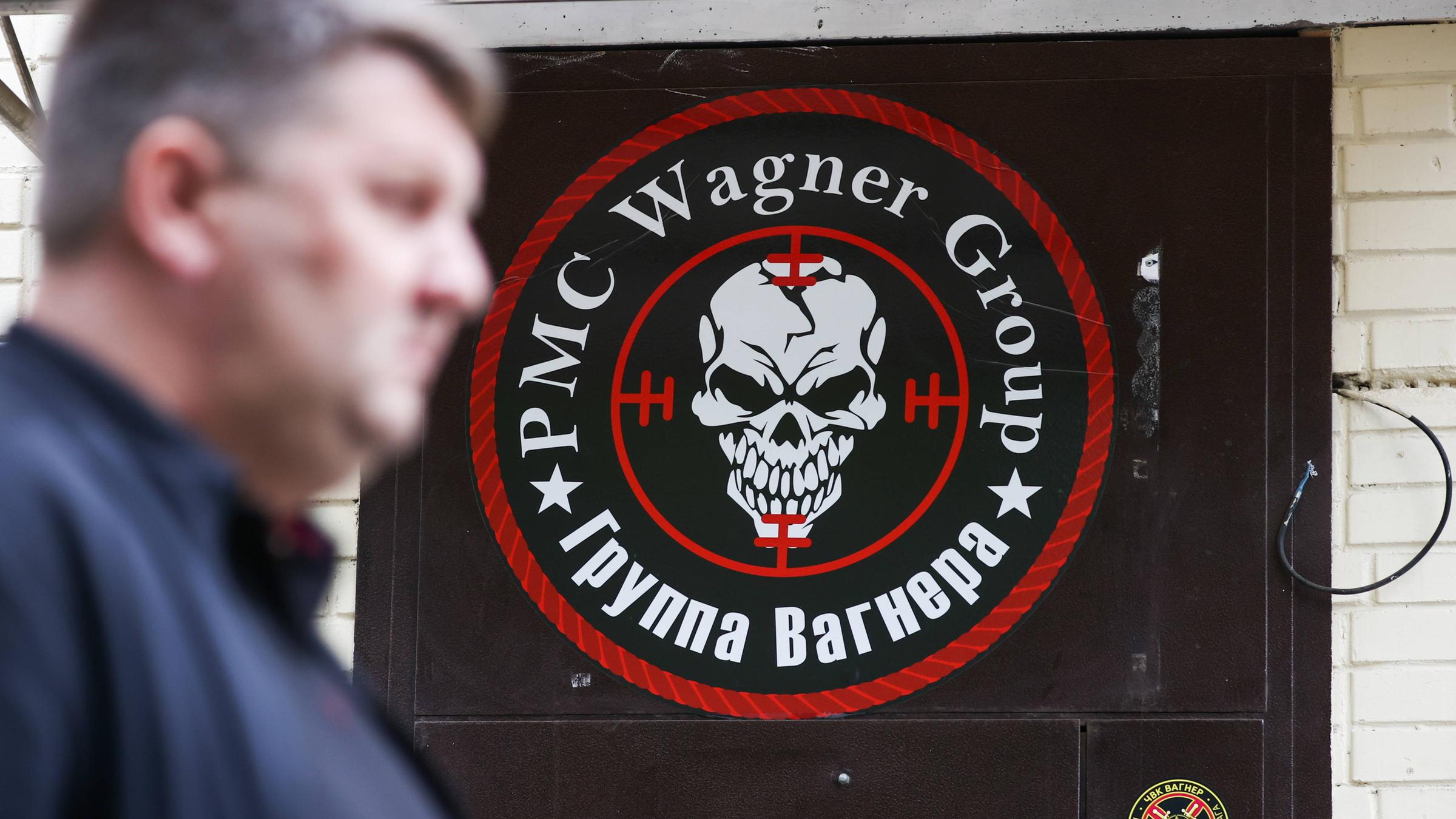 Ein Mann geht an einer Tür vorbei, auf der ein Logo der Gruppe Wagner zu sehen ist. 